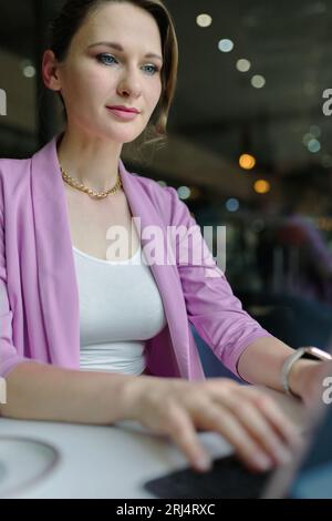 Young woman entrepreneur working on a laptop in a cafe, freelance work concept, vertical Stock Photo