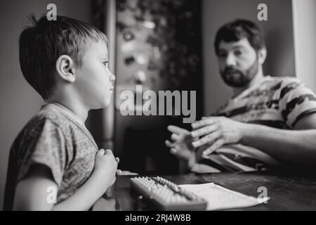 cute little caucasian boy doing his mental arithmetic homework with father sitting next to him at the kitchen table. High quality photo Stock Photo