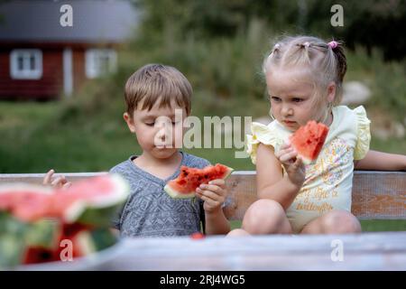 cute caucasian children eating watermelon at the wooden table in countryside. Image with selective focus Stock Photo