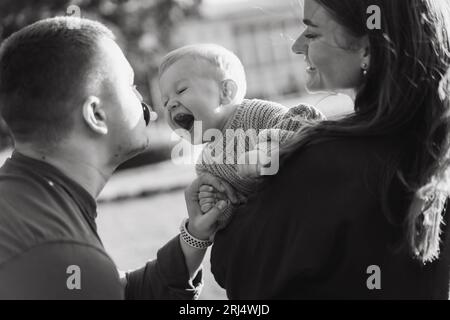 happy family in a park. Dad is holding dummy in mouth. Mother holding baby son trying to take out a pacifier. High quality photo Stock Photo