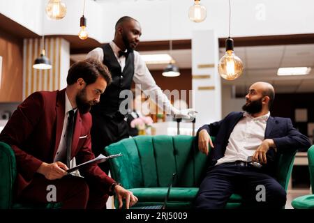 White collar worker reads files in lobby, working on official documents plan while he waits to see accommodation at hotel. Business representative reviewing speech notes, lounge area. Stock Photo