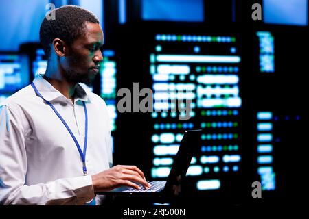Precise engineer inspecting blade servers performing data backups and providing centralized storage. African american specialist maintenancing electric generators ensuring operational continuity Stock Photo