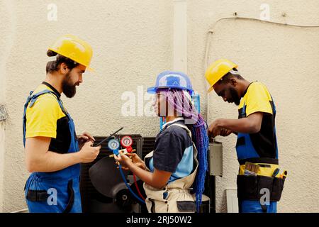 Skilled technicians refilling freon and fixing leaks in external air conditioning unit. Knowleadgeable engineers diagnosing hvac system to prevent refrigerant loss and ensure optimal performance Stock Photo