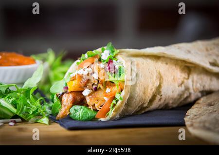 A closeup shot of a wrap filled with chicken on a bed of fresh green lettuce leaves. Stock Photo