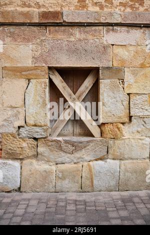 Close up view of stone facade with wooden window blocked with two x-shaped wooden slats Stock Photo