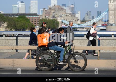 A Just Eat cycle courier riding an e-bike across London Bridge, London, UK.  7 Jun 2023 Stock Photo