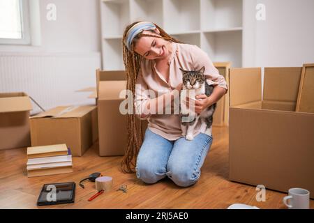 Happy modern ginger woman with braids moving into new home with her pet. Stock Photo