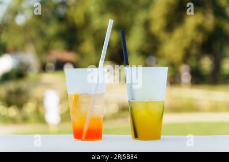 Two different summer cocktails in glasses with straws on a blurred green background. Stock Photo
