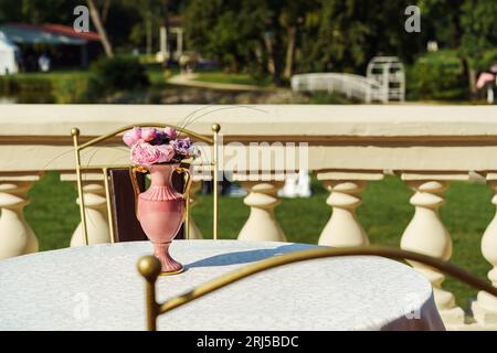 Pink vase with pink flowers on the table on the terrace of a restaurant in the park in summer. Stock Photo