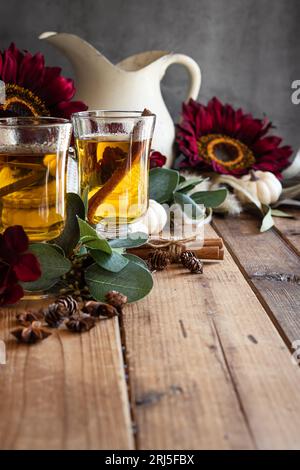 An autumn scene of hot apple cider in pedestal cups with red flowers in the background on a Wooden surface, Stock Photo