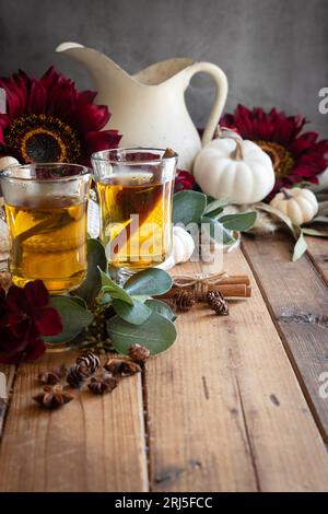 An autumn scene of hot apple cider in pedestal cups with red flowers in the background on a Wooden surface, Stock Photo
