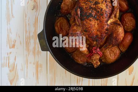 Oven-roasted baked chicken with apples in cast iron skillet pan on the white wooden background food photo tabletop, flat lay view. Stock Photo
