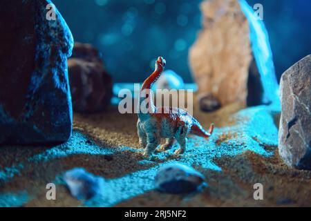 Dinosaur in a rocky gorge at night. Creative scenery with a small miniature. Stock Photo