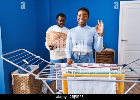 Young african american couple hanging clothes at clothesline doing ok sign with fingers, smiling friendly gesturing excellent symbol Stock Photo