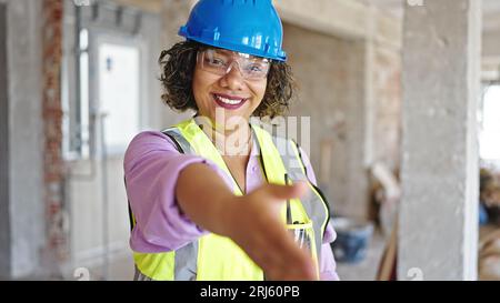 Young beautiful latin woman builder smiling confident doing thumbs up gesture at construction site Stock Photo