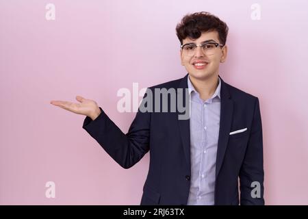 Young non binary man with beard wearing suit and tie smiling cheerful presenting and pointing with palm of hand looking at the camera. Stock Photo