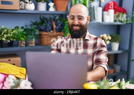 Young bald man florist smiling confident using laptop at flower shop Stock Photo
