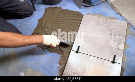 Bathroom renovation with tile adhesive. A worker lays dark gray ceramic floor tiles on an adhesive surface. Tile adhesive for bonding ceramic tiles to Stock Photo