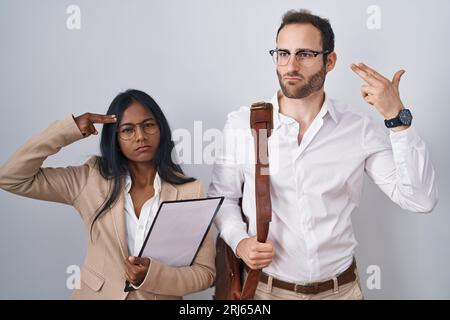 Interracial business couple wearing glasses shooting and killing oneself pointing hand and fingers to head like gun, suicide gesture. Stock Photo