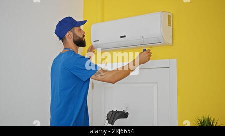 Young hispanic man technician repairing air condition machine standing on ladder at home Stock Photo