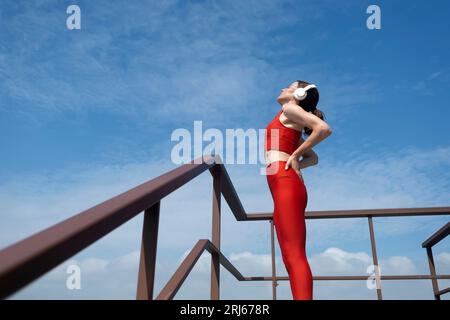 female athlete in sportswear wearing wireless headphones and listening to music while out exercising. Outdoor fitness concept. Stock Photo