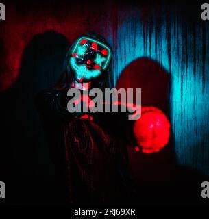 A crazy girl wearing an ominous neon mask with a wired baseball bat standing in a dark room Stock Photo