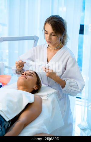 Cosmetologist preparing client for cosmetic procedures by putting disposable cap on woman head Stock Photo