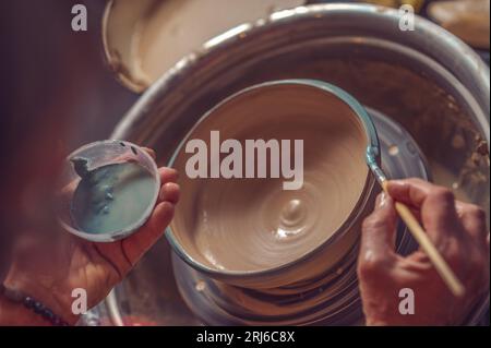 Closeup of woman painting clay mug, coloring pottery in workshop with a paintbrush. Stock Photo