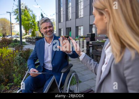 Woman and man in wheelchair waving hands saying good bye after bussines meeting Stock Photo
