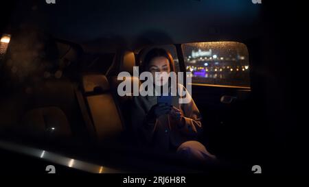 Stylish luxurious woman in suit sitting in black car at night in the passenger seat Stock Photo