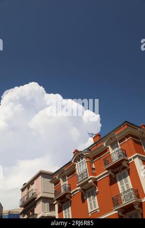 A low-angle view of a vibrant terracotta building standing against a large white cloud Stock Photo