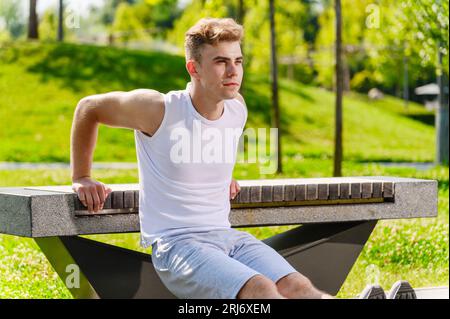 Athlete man doing push-ups on bench in park. Training triceps workout concept fitness, sport. Stock Photo