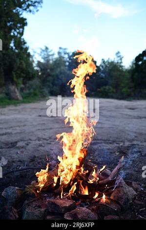 A dramatic image of a raging fire burning next to some rocks and a small body of water in a natural setting Stock Photo
