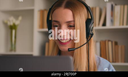Happy Caucasian smiling woman in headset talking conference call video chat speak at computer laptop at home office job interview distance language Stock Photo