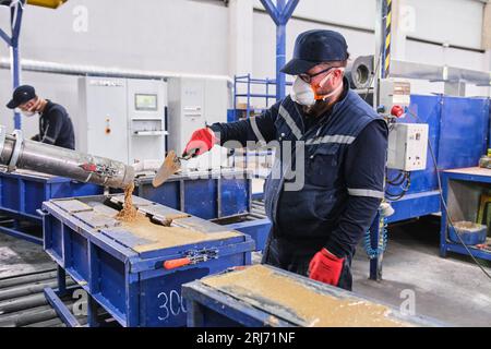 factory worker pours cement mixture into a mold and flattens it out with a tool. Stock Photo