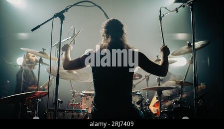 A man on a stage performing on the drums during a concert, shot from back Stock Photo
