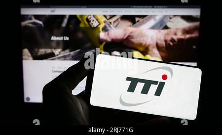 Person holding smartphone with logo of Techtronic Industries Company Limited (TTI) on screen in front of website. Focus on phone display. Stock Photo