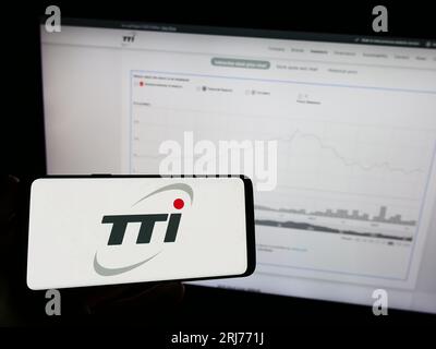 Person holding mobile phone with logo of Techtronic Industries Company Limited (TTI) on screen in front of web page. Focus on phone display. Stock Photo