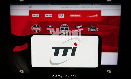 Person holding cellphone with logo of Techtronic Industries Company Limited (TTI) on screen in front of business webpage. Focus on phone display. Stock Photo