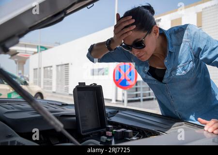 Concerned woman checking car fuses, struggling with a broken-down sports car, vehicle maintenance issues and frustration in an emergency situation Stock Photo