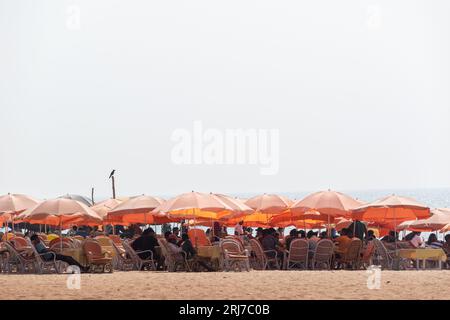 Calangute, Goa, India - January 2023: Orange umbrellas and wicker chairs at a seaside restaurant shack on a beach in Calangute. Stock Photo