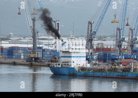 Black smoke as air pollution coming out from funnel of tanker vessel leaving the port. Stock Photo