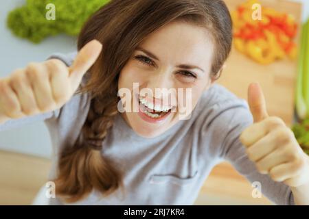 Happy young housewife in modern kitchen showing thumbs up Stock Photo