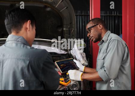 Mechanics using application to check if car parts and engine works good Stock Photo