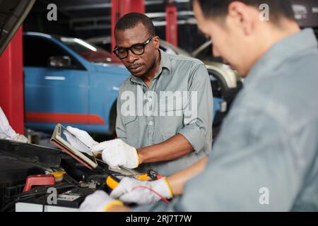 Team of mechanics using multimeter when checking car engine Stock Photo