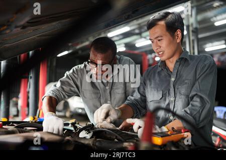 Team of car mechanics in uniform checking car engine Stock Photo