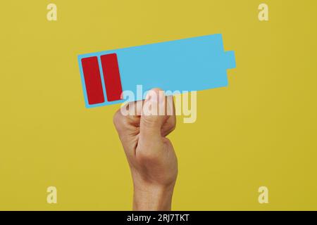 closeup of a man holding a depiction of a battery with a low charge level on a yellow background Stock Photo