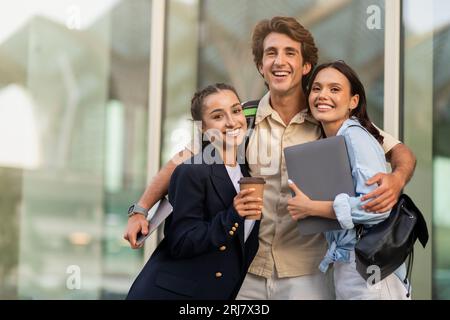 Happy guy and two ladies students embracing and smiling outdoor Stock Photo