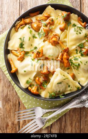Triangular Italian dumplings pasta triangoli with chanterelle mushrooms, onion and herbs close-up in a plate on the table. Vertical top view from abov Stock Photo
