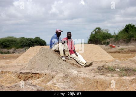 Two men are sitting on top of a mound of sand as they rest from digging for sand. Sand mining is illegal in most parts of the country. Harare, Zimbabwe. Stock Photo